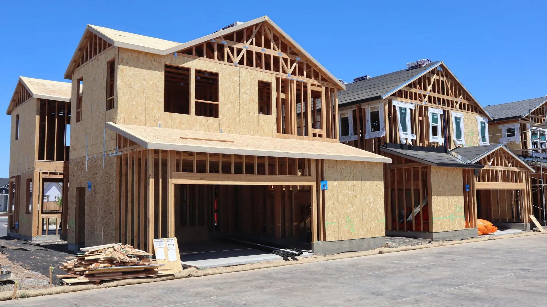 Two-story houses in wood framing and sheathing under a clear sky