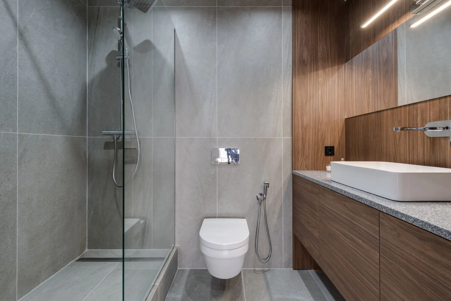 Walk-in glass shower beside a wood vanity with a vessel sink
