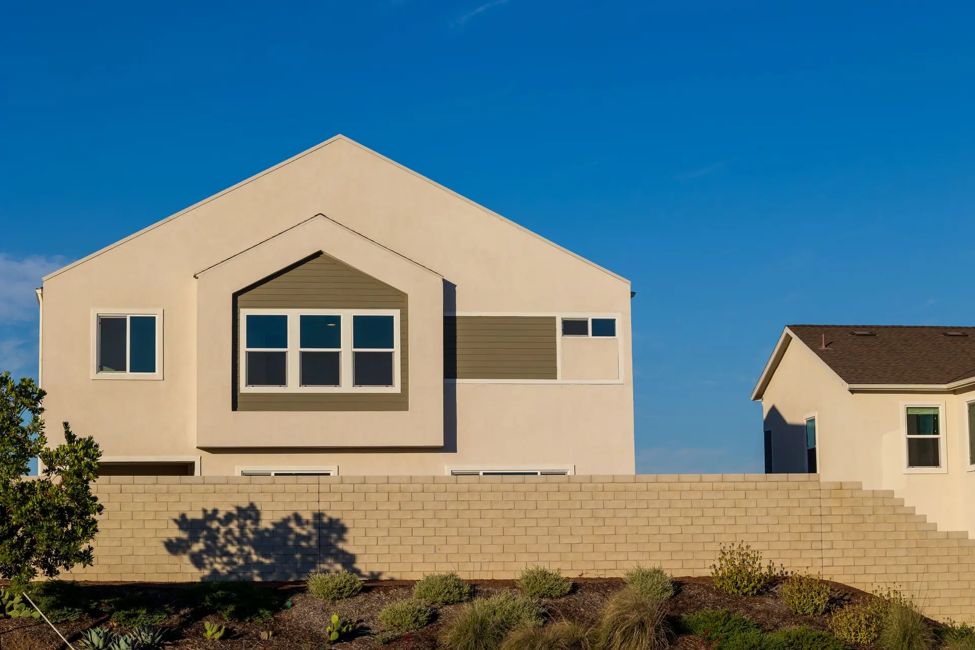 Smooth stucco house with a gable window above a block garden wall